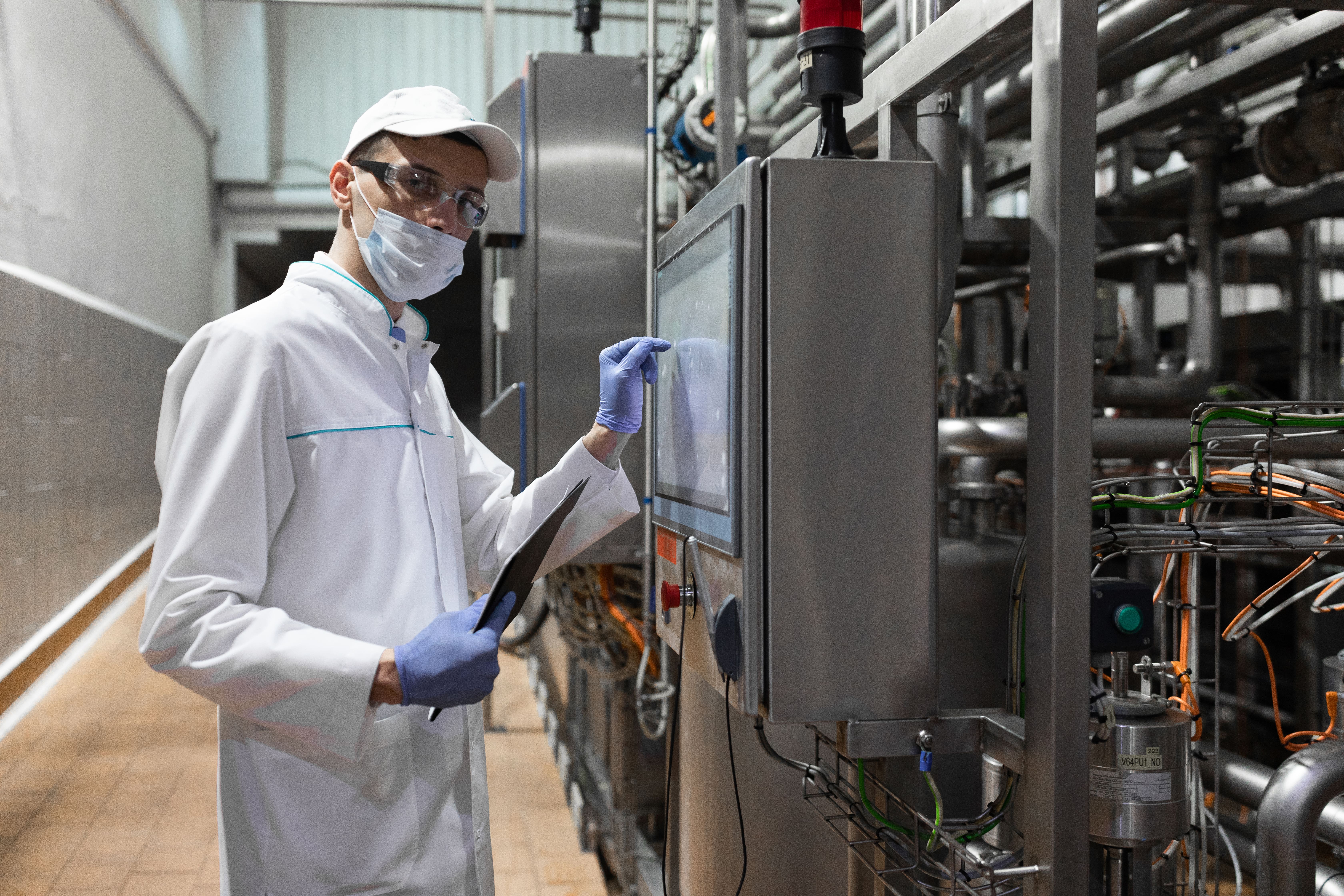 concentrated technologist taking necessary notes with help digital tablet while standing production department dairy factory inspector carries out control cheese factory